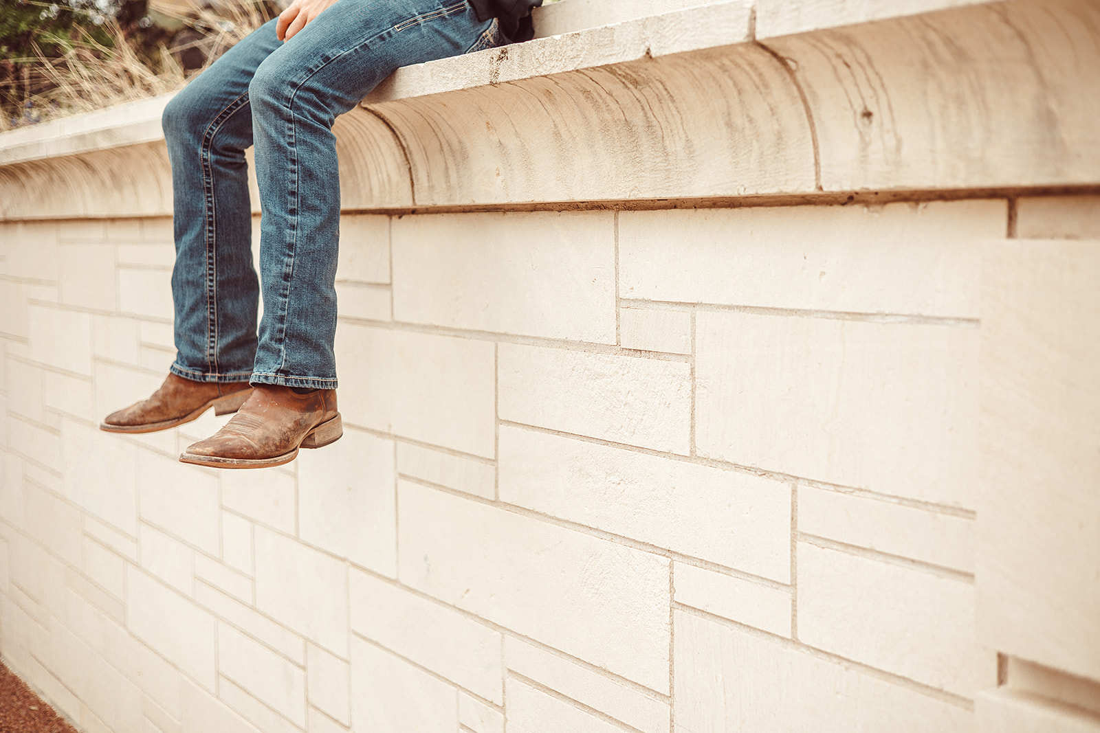A student's cowboy boots and jeans dangle off a stone ledge on the UT Austin campus | SMART Housing Austin